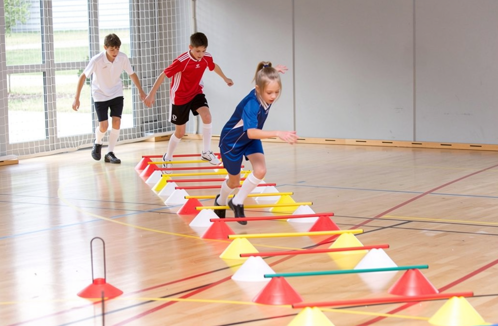 Kinderen oefenen fijnmotoriek met een kleurrijk parcours van pionnen in een sportzaal.