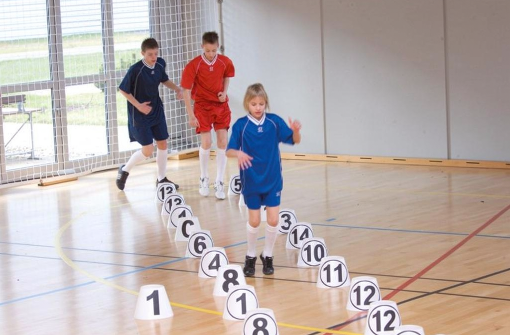 Kinderen oefenen motoriek op een pionnenparkoers in de gymzaal.