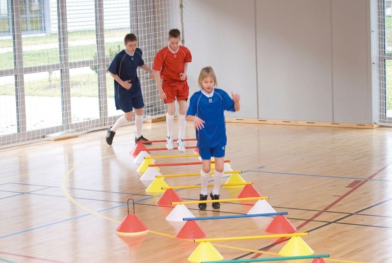 Kinderen oefenen motoriek met pionnen en latten in een gymzaal.