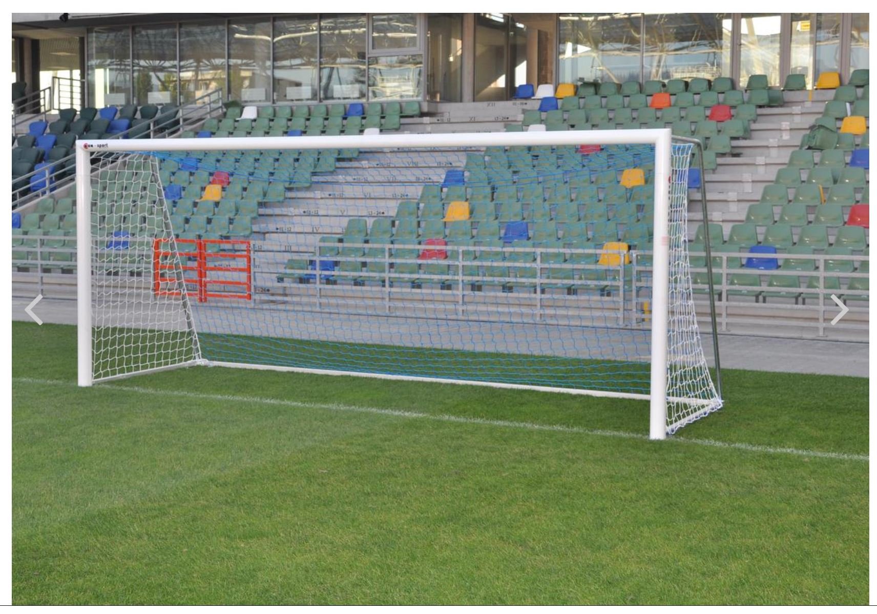 Een voetbaldoel op een grasveld voor een stadion met lege, kleurrijke tribunes.